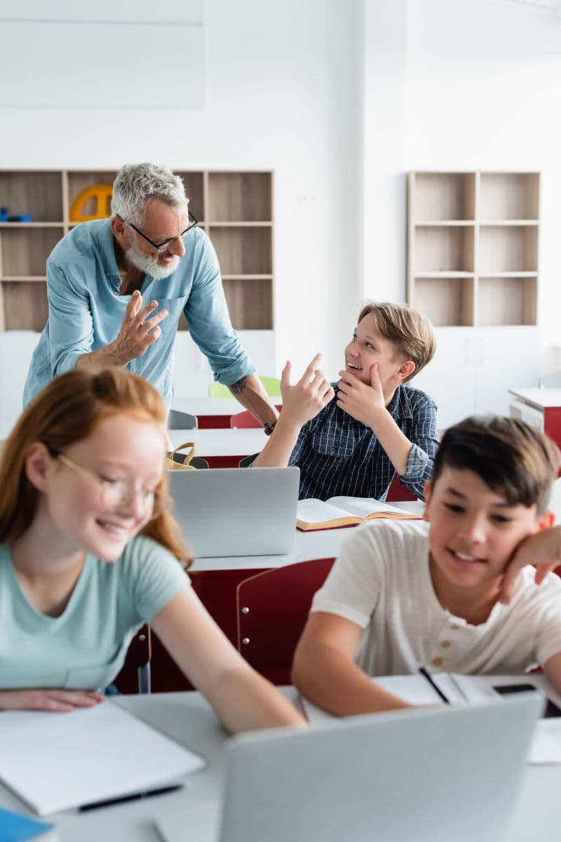 Lehrer interagiert mit Schülern, die an Laptops arbeiten.
